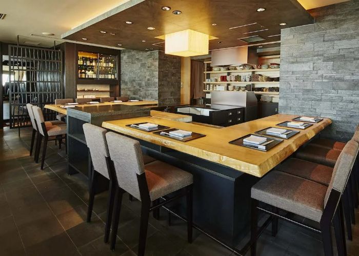 Counter seating at XEX ATAGO GREEN HILLS, showing grey dining chairs surrounding a square cooking area.